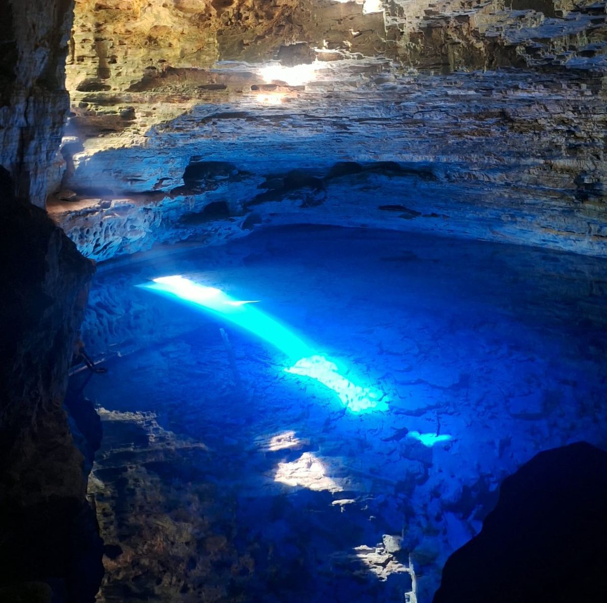 Feixe de luz azul intenso iluminando as águas cristalinas do Poço Encantado, Chapada Diamantina